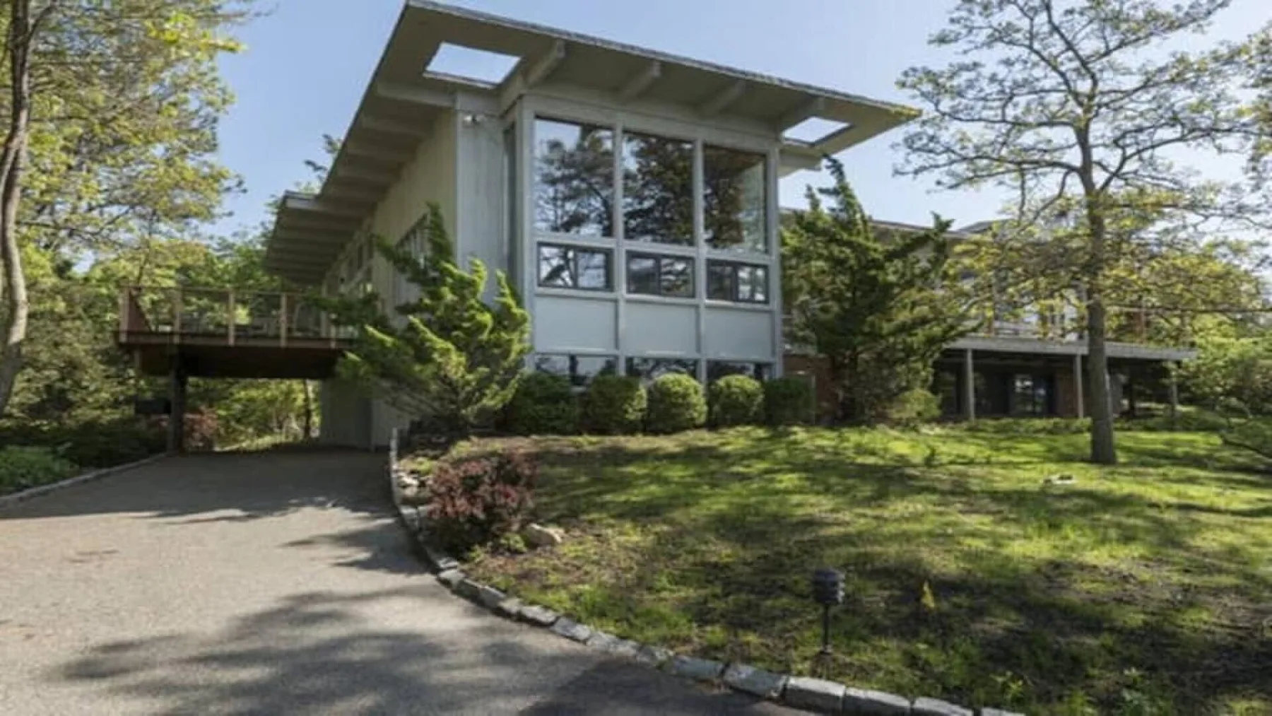 Una casa moderna está entre árboles junto a una entrada curva.