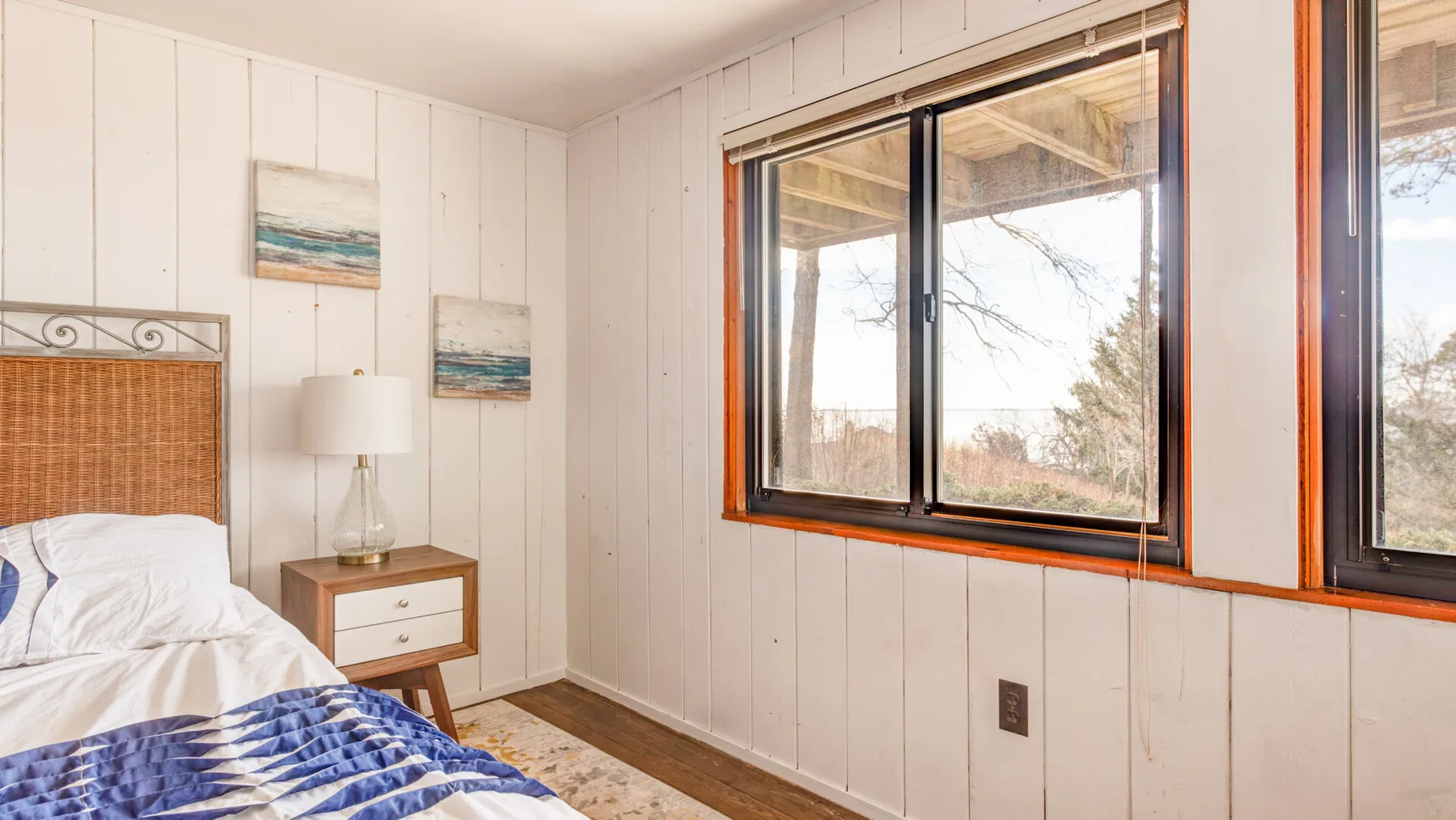 Un dormitorio con una cama, una mesita de noche y ventanas grandes.
