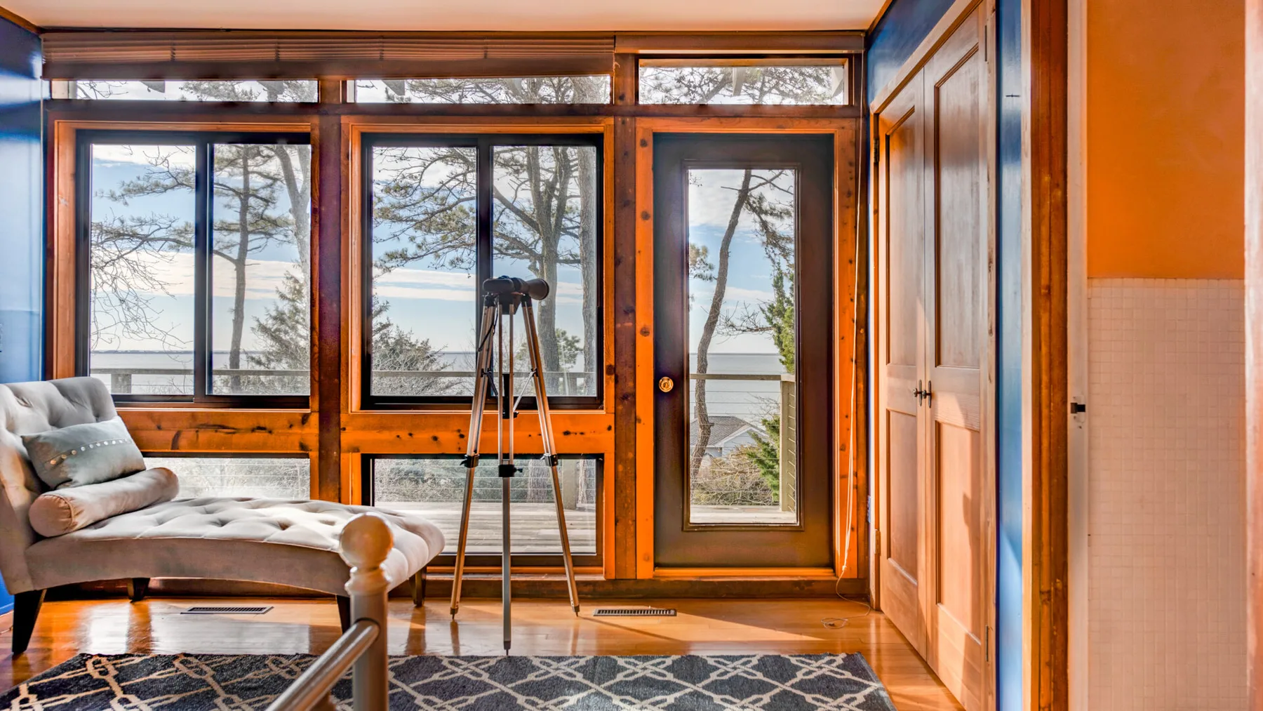 A sunroom with large windows, a seating area, and a tripod by the door.