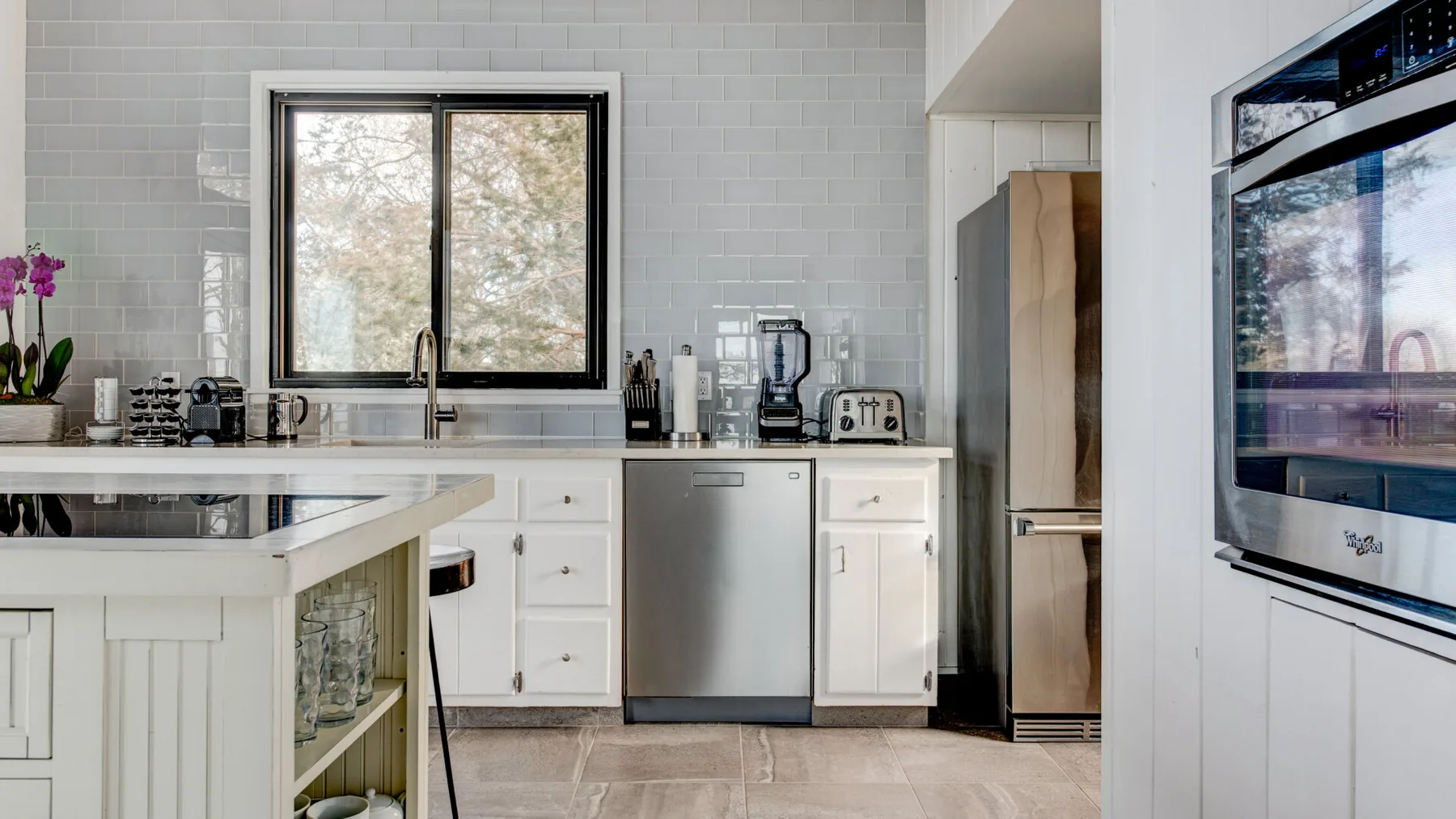 Una cocina luminosa con gabinetes blancos, un fregadero central y electrodomésticos de acero inoxidable.