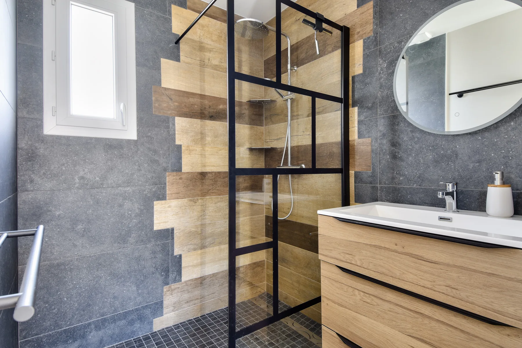 A modern bathroom with a glass shower, vanity, and round mirror.