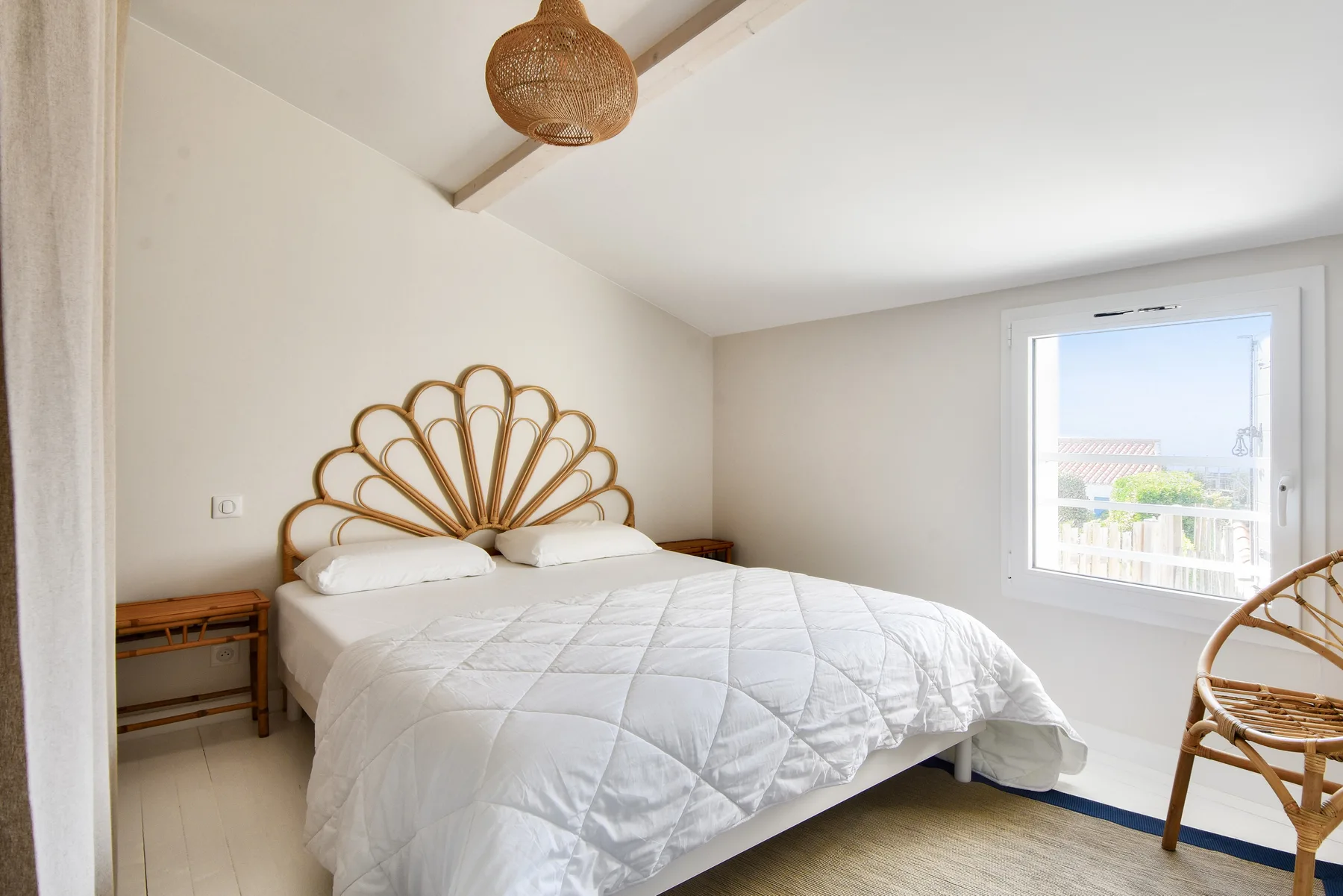 A bright bedroom with a bed beneath a woven pendant light.