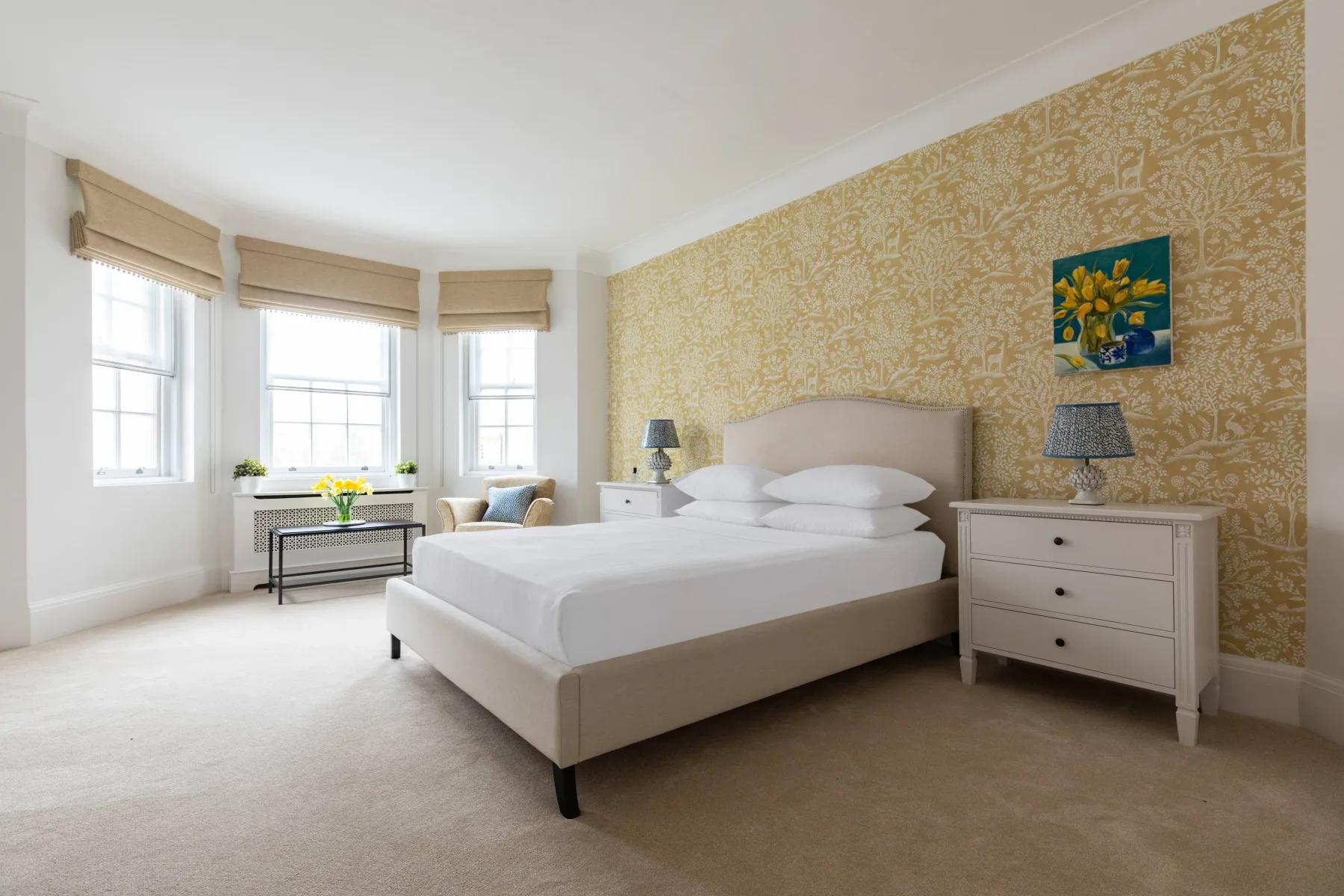 A bright bedroom with a neatly made bed and patterned wallpaper.