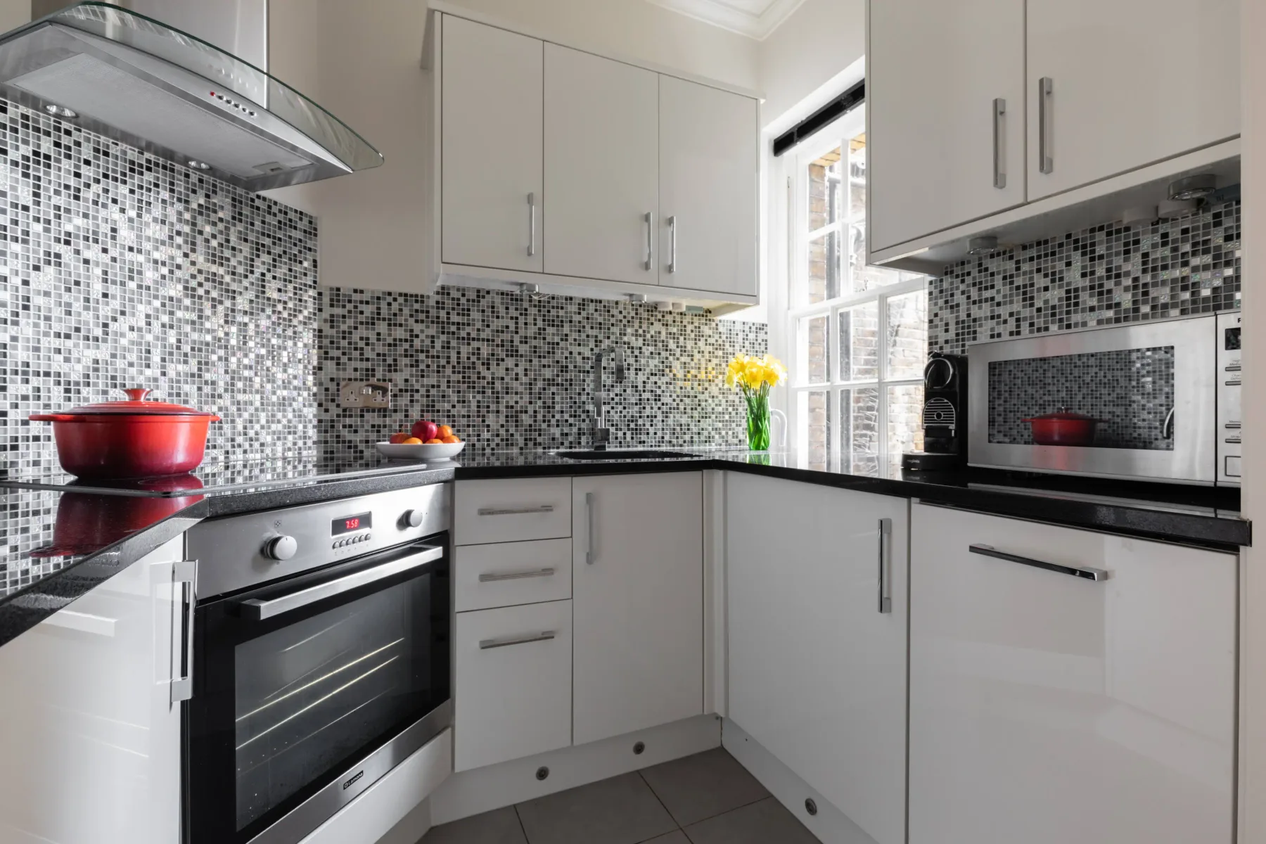 A bright modern kitchen with white cabinets, dark countertops, and mosaic tile.