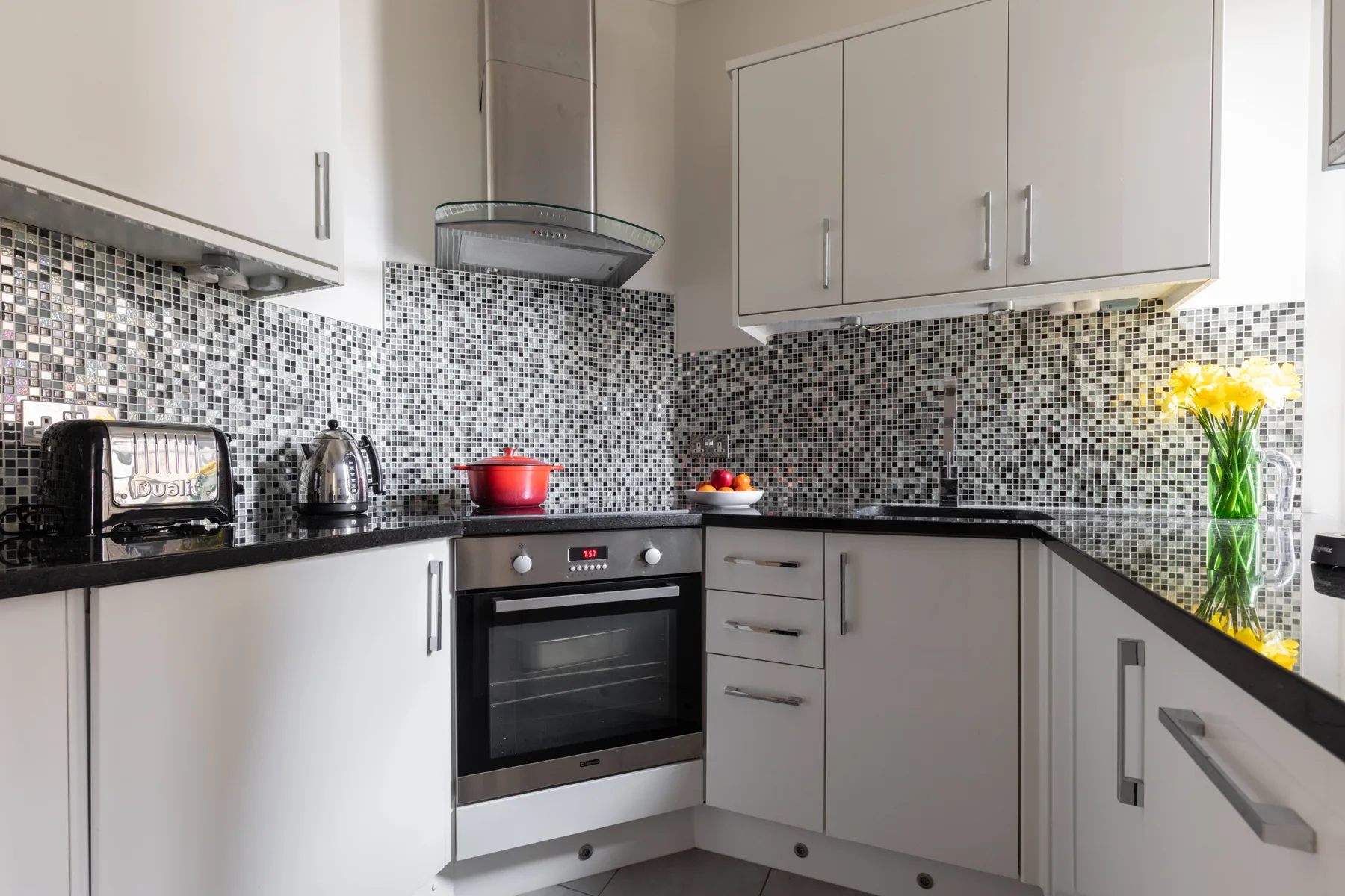 A bright kitchen with white cabinetry, dark countertops, and a mosaic backsplash.