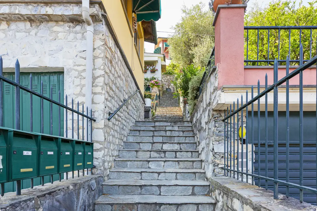 Stone steps rise between buildings, with green mailboxes along the left wall.