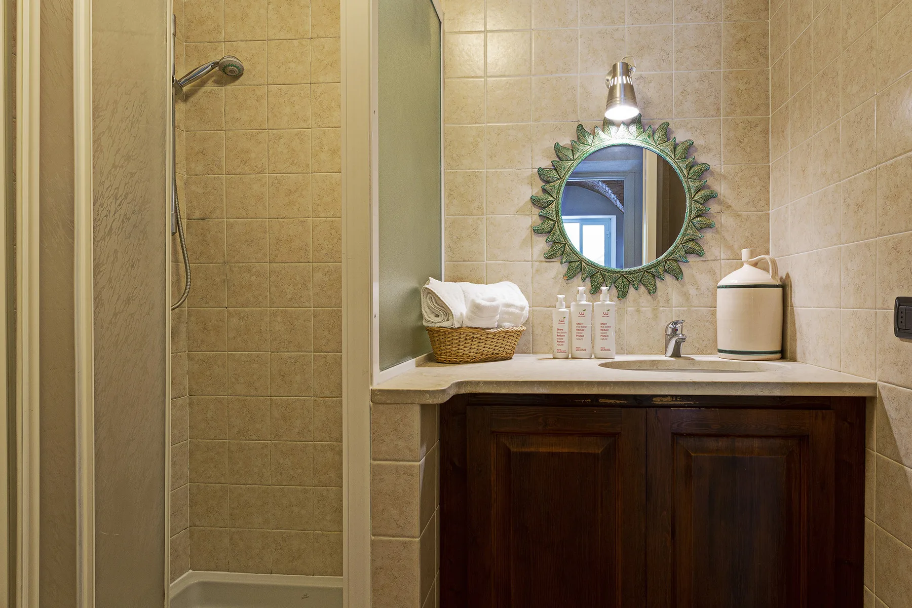A tiled bathroom with a shower, sink, and round mirror.