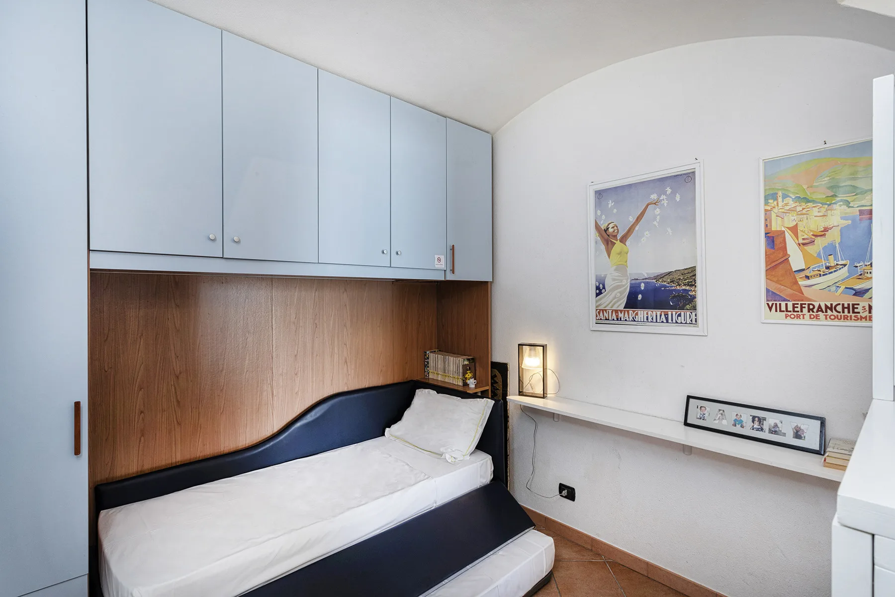 A bedroom with a bed beneath built-in cabinets and colorful wall posters.