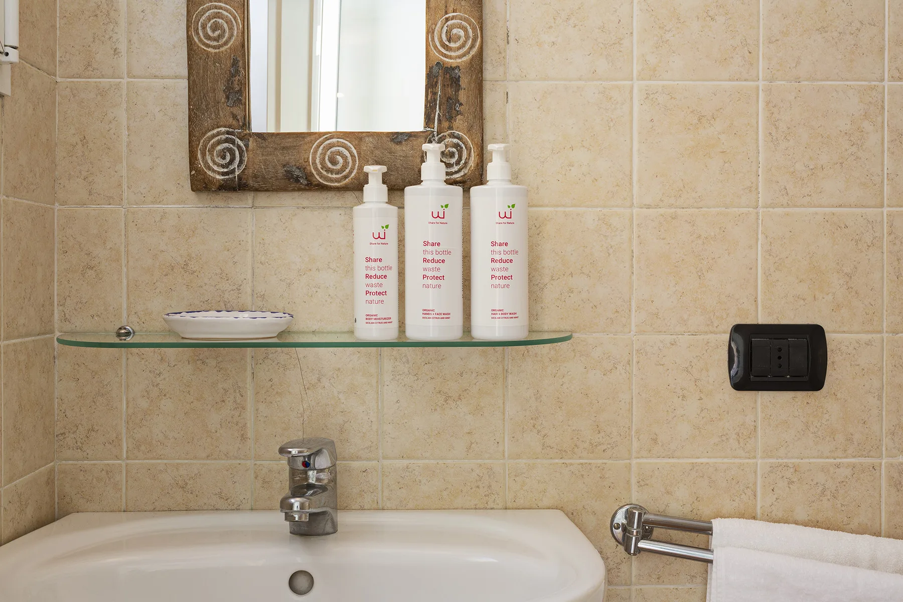 A tiled bathroom sink with a wall mirror, toiletries, and a towel.
