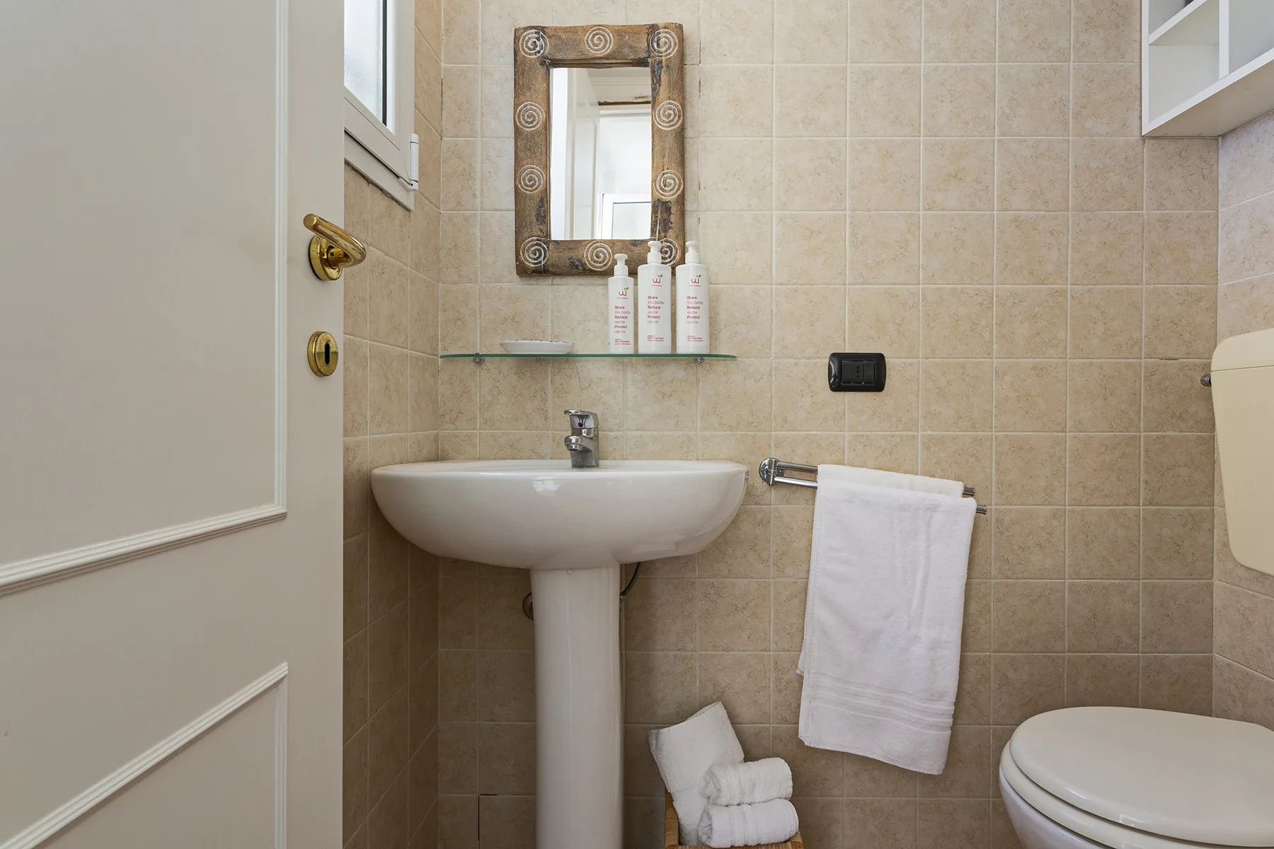 A tiled bathroom with a pedestal sink, mirror, and white towels.