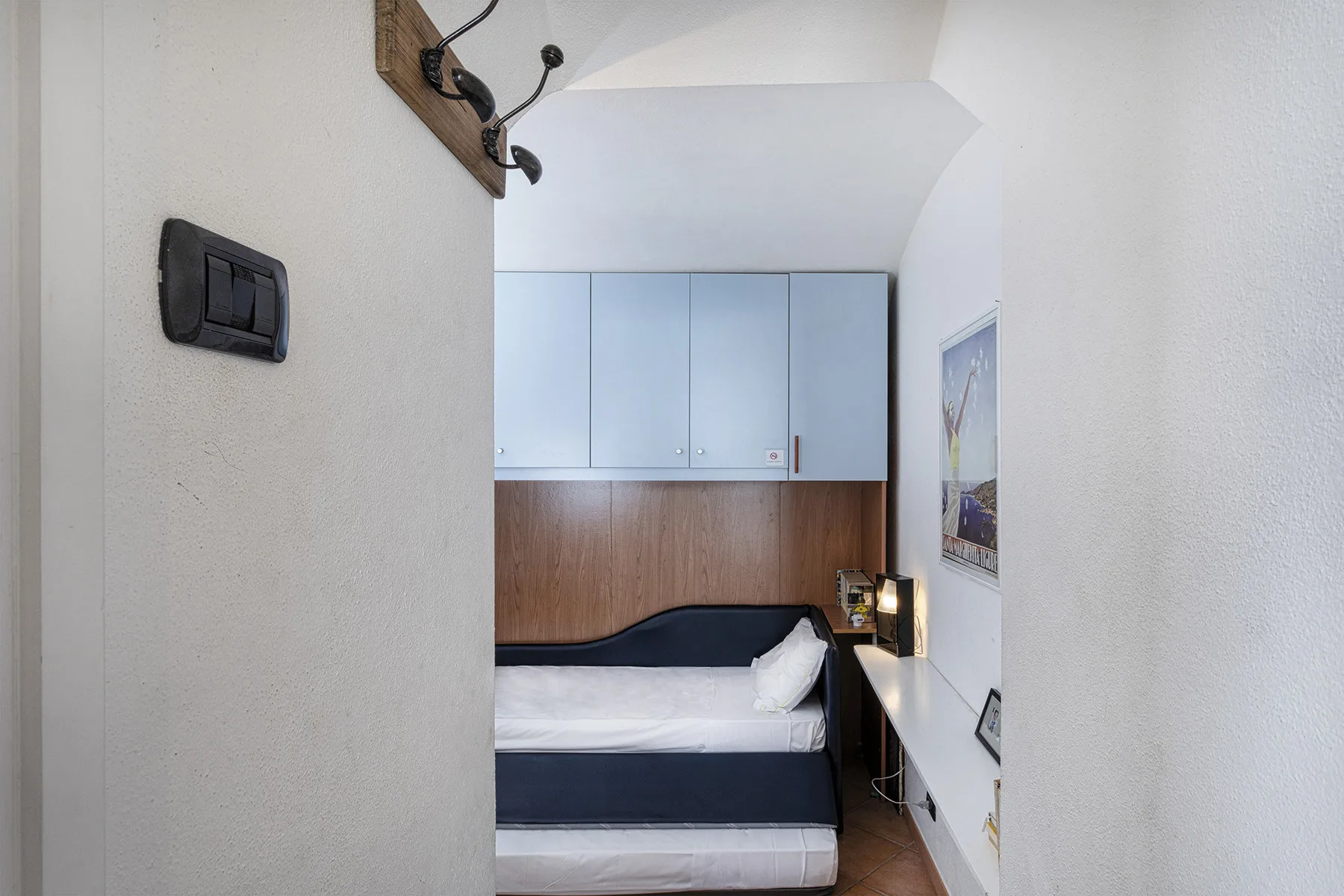 A bedroom with a bed beneath overhead cabinets and a desk beside it.