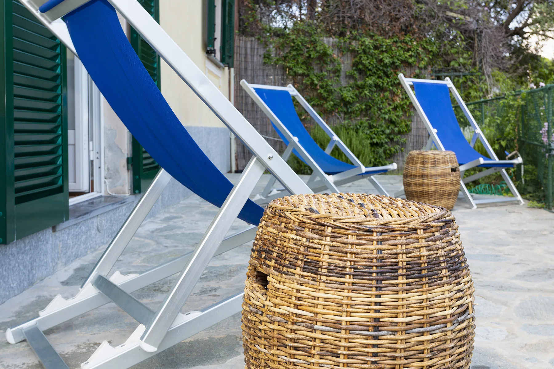 Blue lounge chairs and woven baskets sit on a patio beside a building.