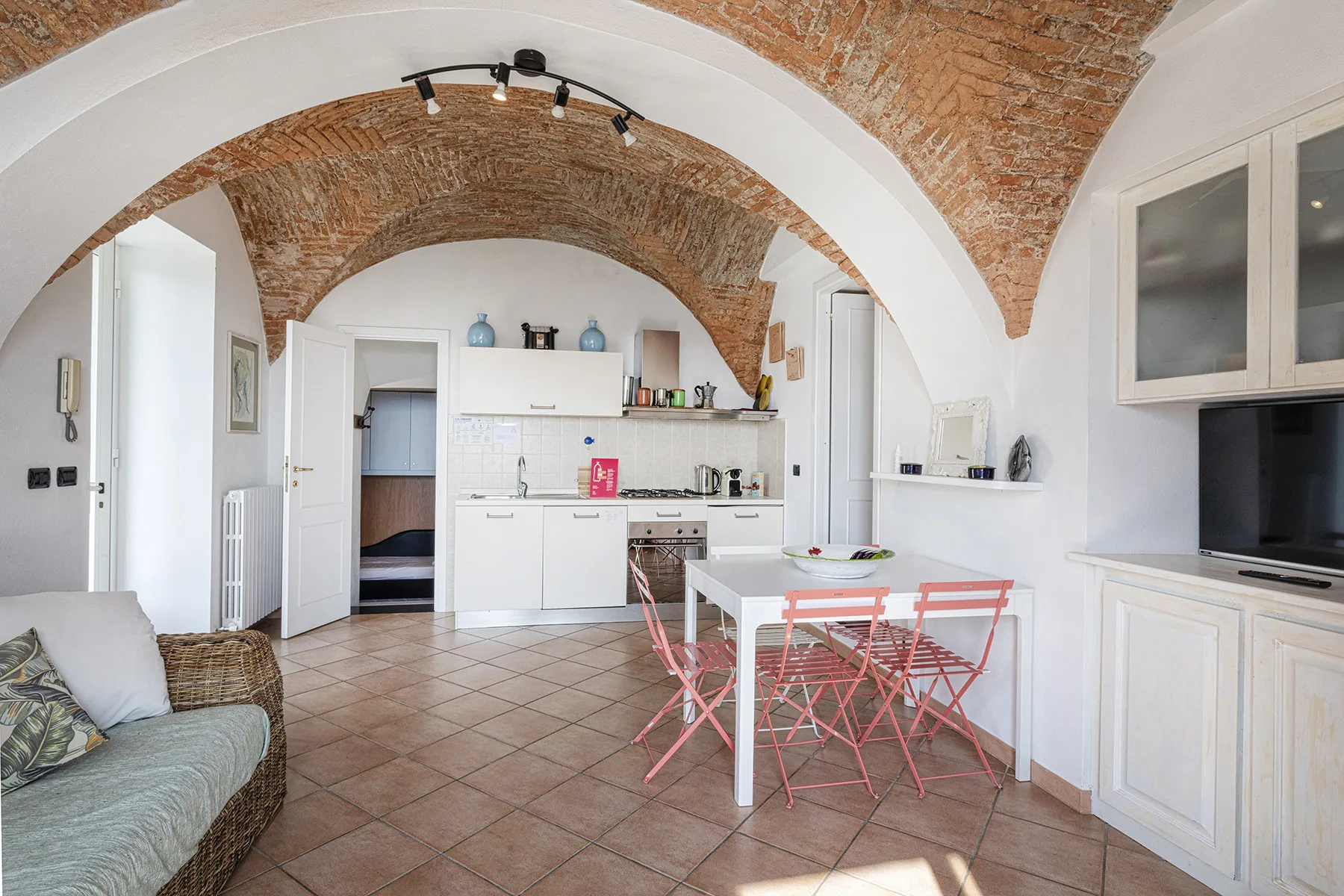 A bright kitchen and dining area has white cabinetry and a table beneath brick arches.