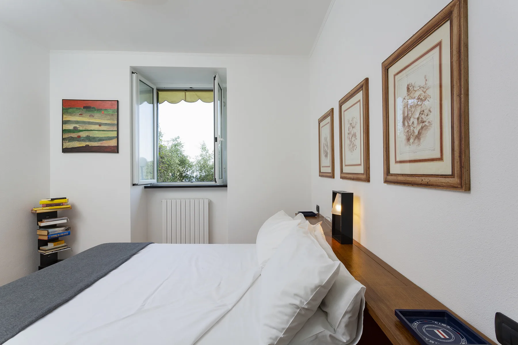 A bedroom with a bed, framed artwork, and an open window.