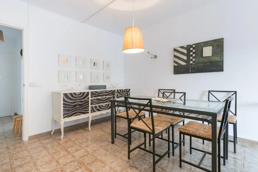 Comedor con mesa de vidrio, asientos y cuadros en paredes blancas.