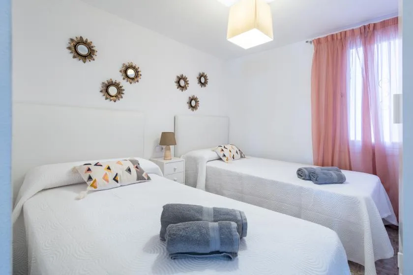 Un dormitorio luminoso con dos camas y cortinas rosas junto a la ventana.
