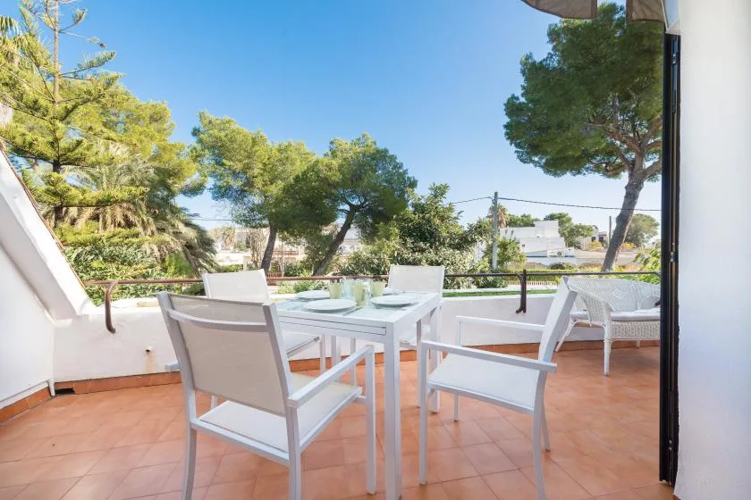 A tiled outdoor terrace has a white dining table and seating beneath the trees.
