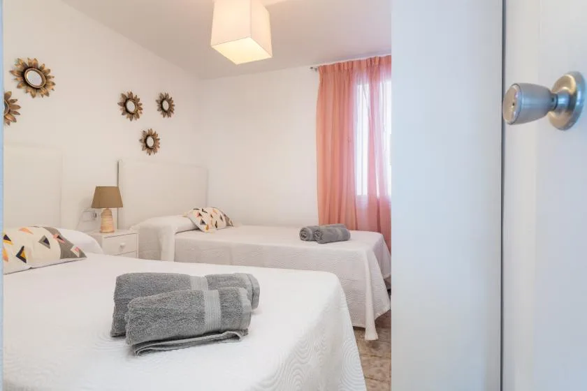 Un dormitorio luminoso con dos camas, toallas dobladas y cortinas rosas.