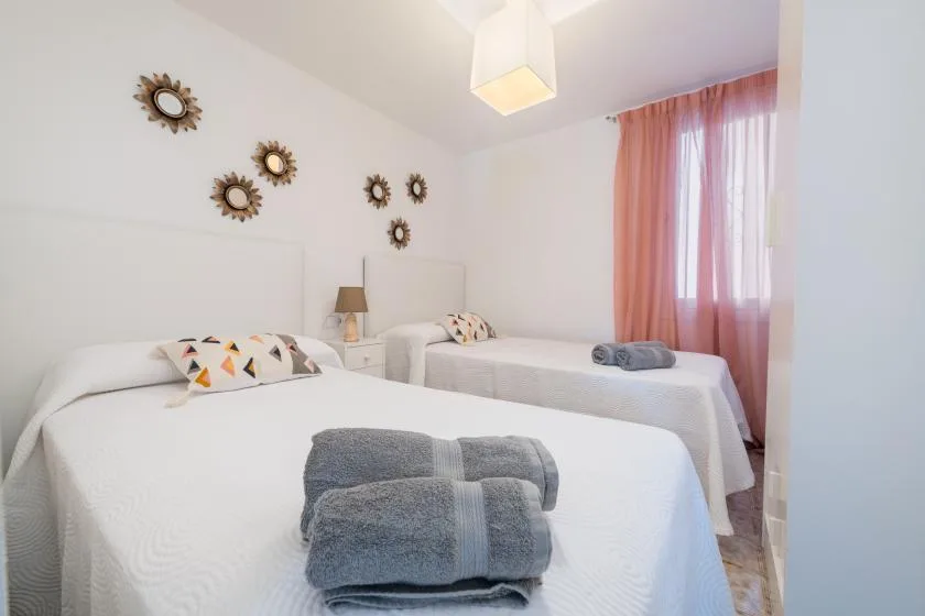 Un dormitorio luminoso con dos camas y cortinas rosas.