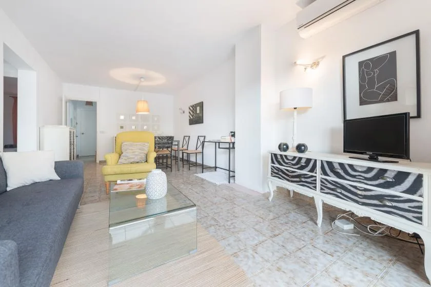 A bright living room with seating, a glass coffee table, and a television.
