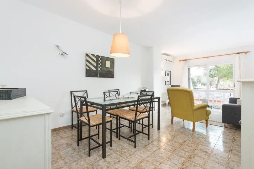 Una luminosa zona de comedor y estar con una mesa y asientos junto a grandes ventanas.