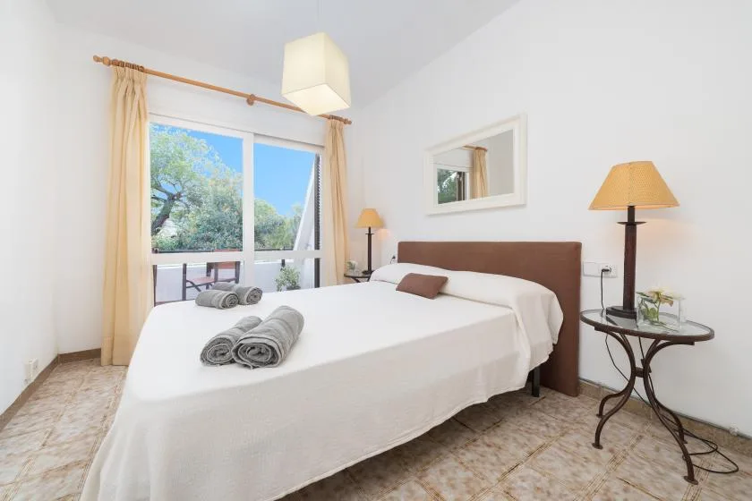 Un dormitorio luminoso con una cama grande, una mesita y puertas de cristal hacia la vegetación.