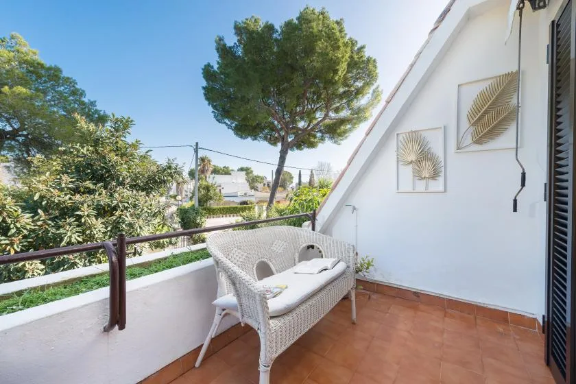 Una terraza soleada con asientos de mimbre, plantas y cuadros botánicos en la pared.