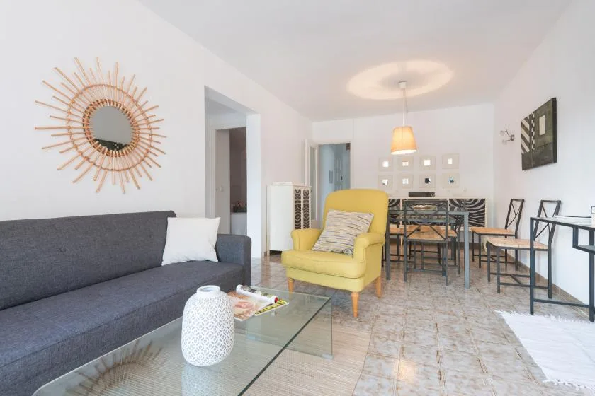 Una luminosa sala de estar y comedor con un sofá gris y un sillón amarillo.
