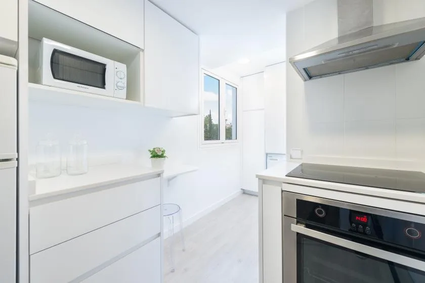 Una cocina blanca y luminosa con horno, placa de cocina y ventana.
