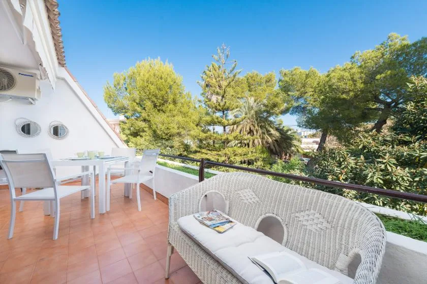 A sunny terrace with outdoor seating overlooks leafy trees beneath a clear blue sky.