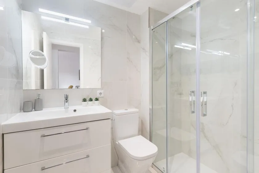 Un baño luminoso con lavabo, inodoro y ducha de vidrio.