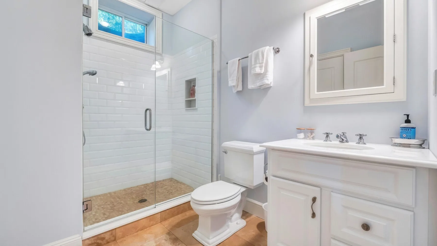 A bright bathroom with a glass shower, white vanity, and toilet.