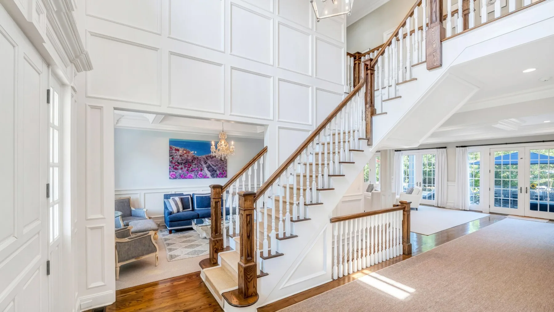 A bright interior features a sweeping staircase beside a living room.