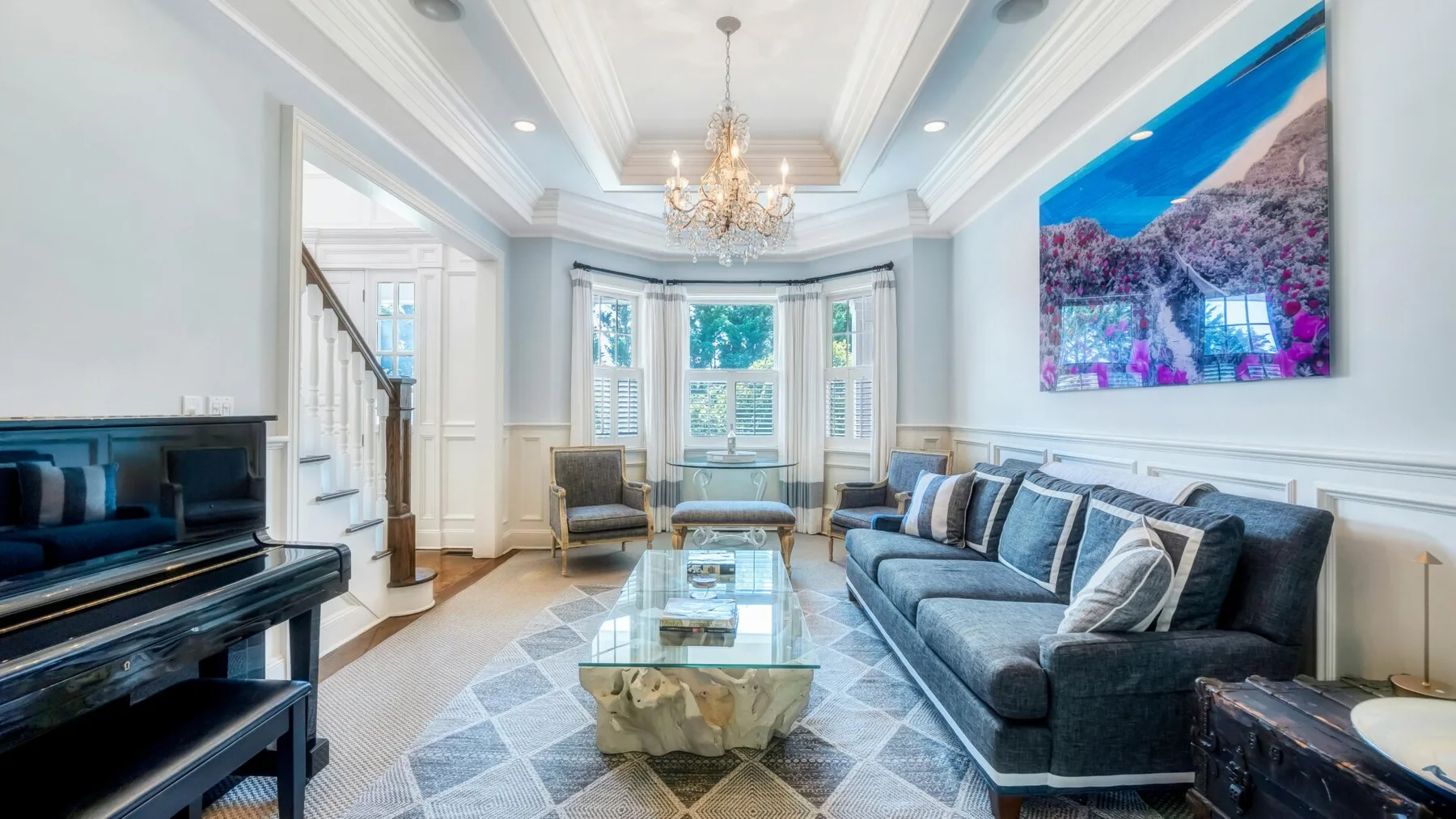 A bright living room with a sectional sofa, glass coffee table, and large wall-mounted screen.