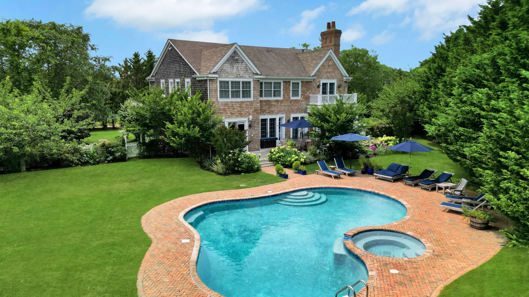 A landscaped backyard features a swimming pool and a large house.
