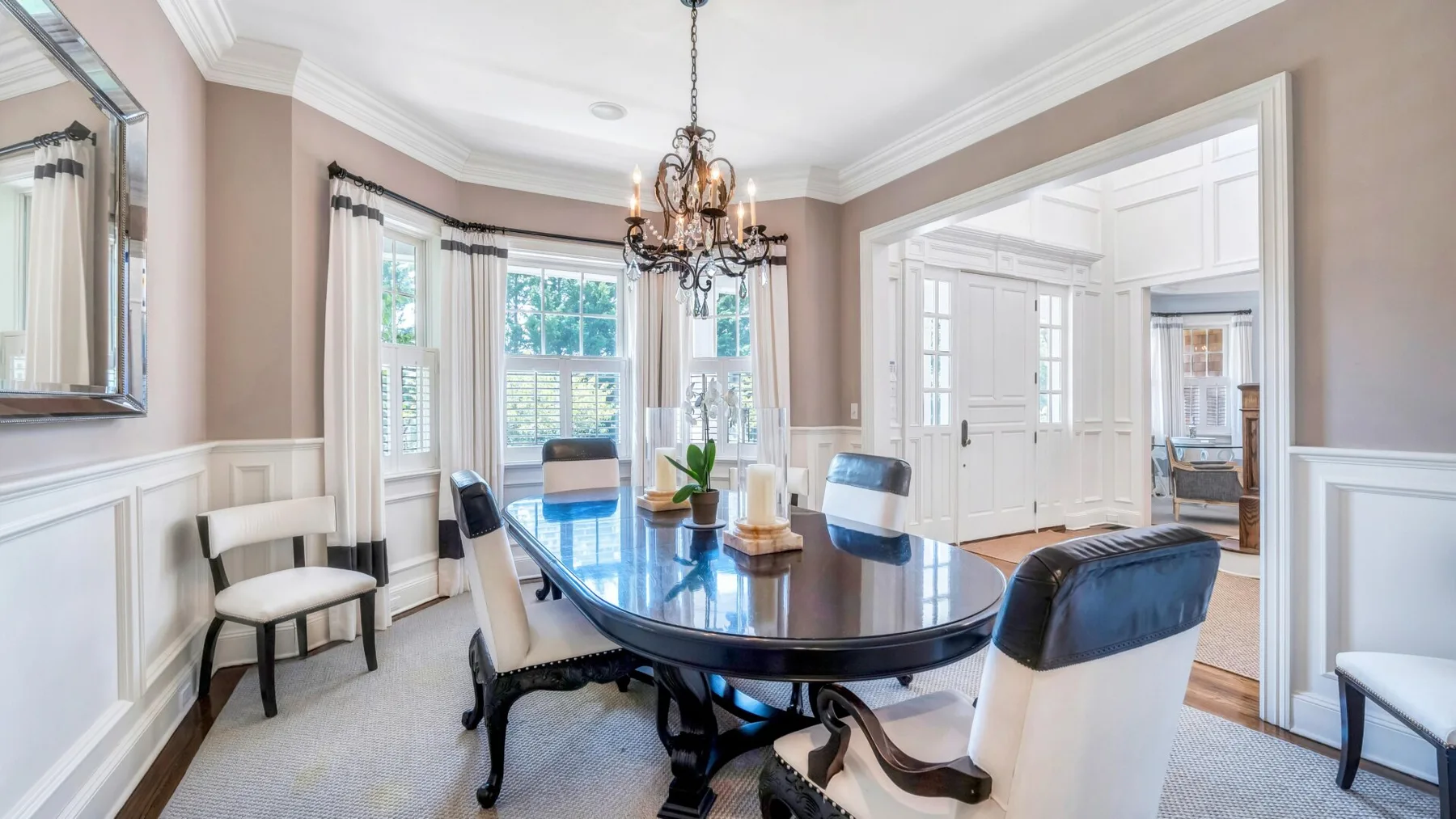 A formal dining room with a dark dining table, chairs, and large windows.