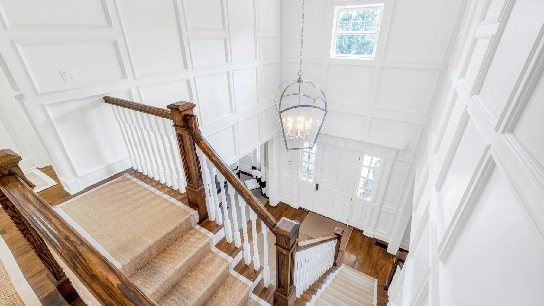 A bright stairwell with wooden railings and a hanging chandelier.