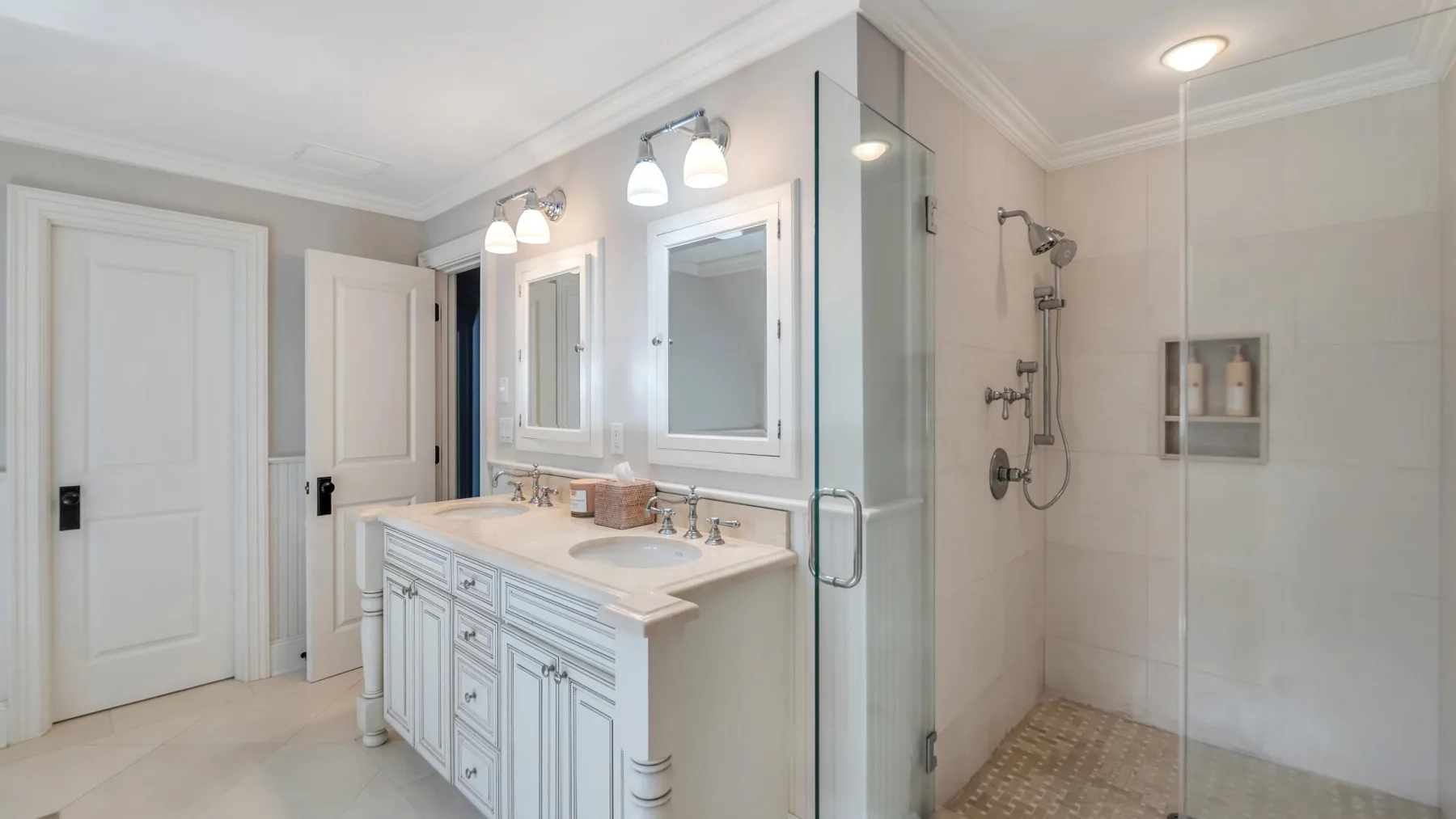 A bright bathroom with a double vanity and a glass-enclosed shower.