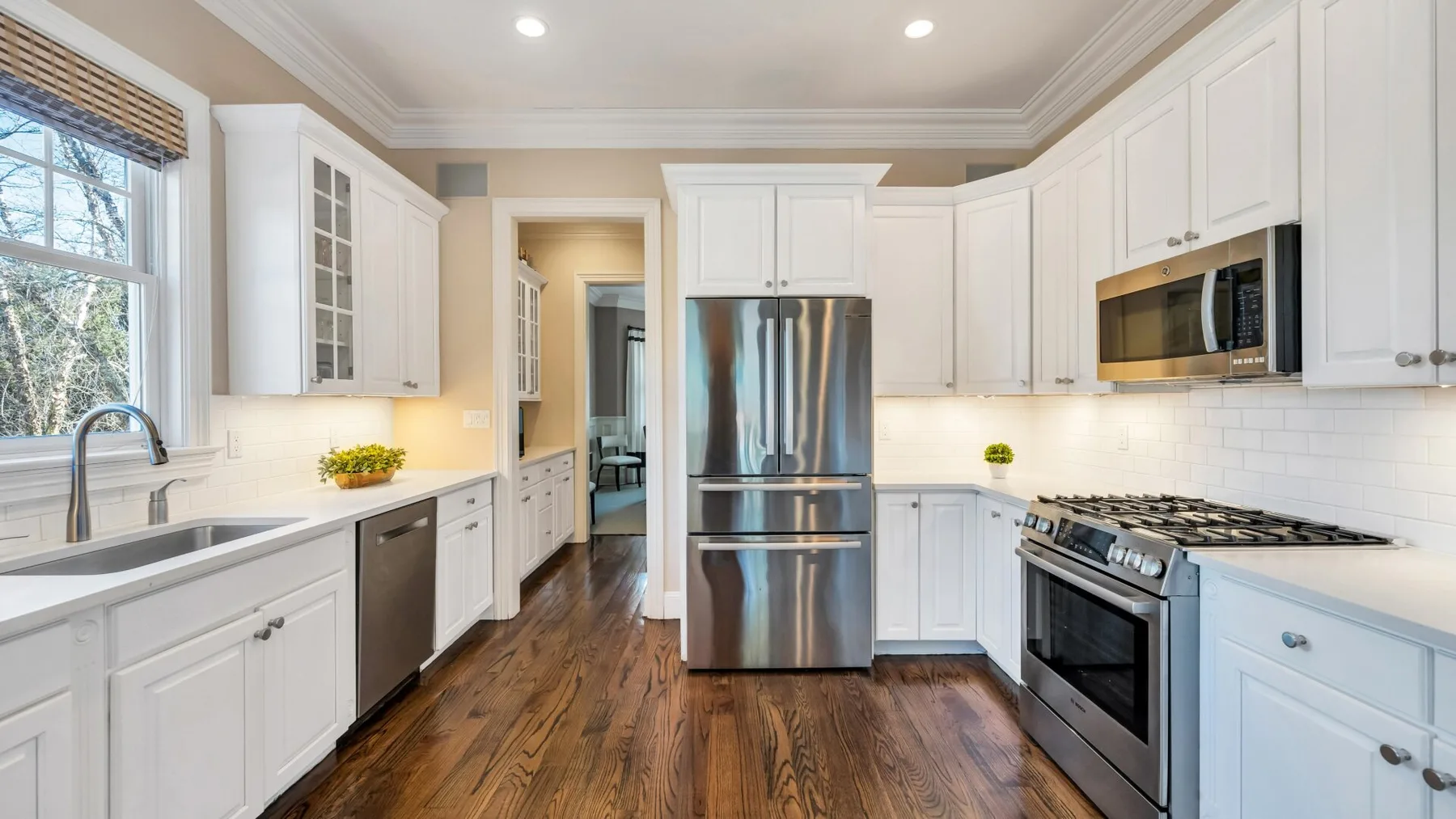 A bright kitchen with white cabinets, stainless steel appliances, and wood flooring.