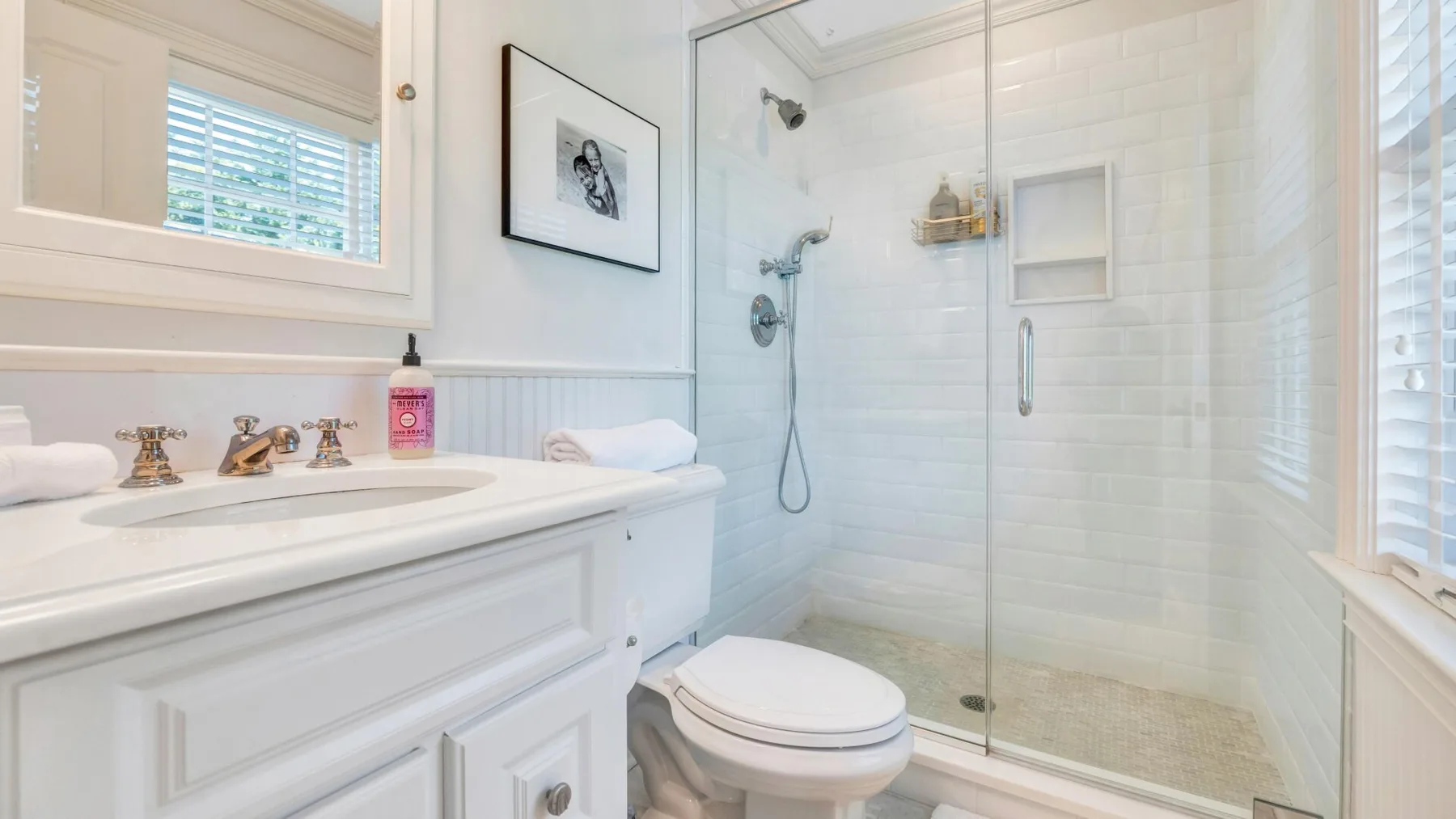 A bright bathroom with a vanity, toilet, and glass-enclosed shower.