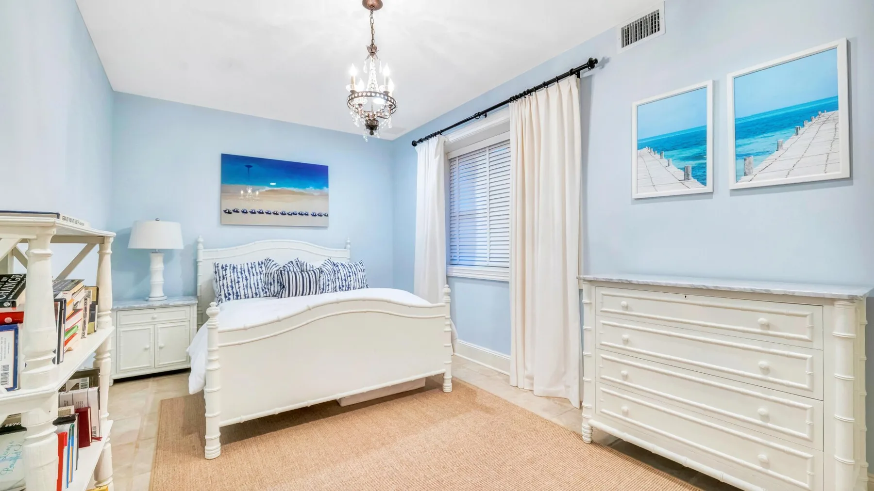 A light blue bedroom with a white bed, dresser, and beach-themed wall art.
