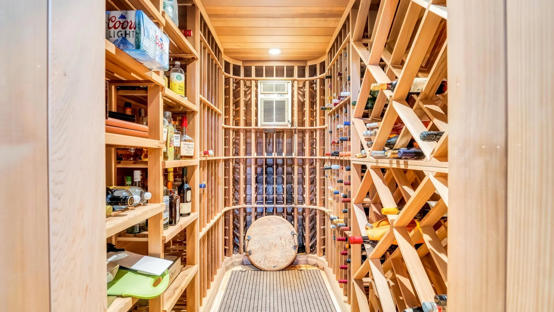 A narrow wine cellar with wooden shelving and a barrel at the far end.