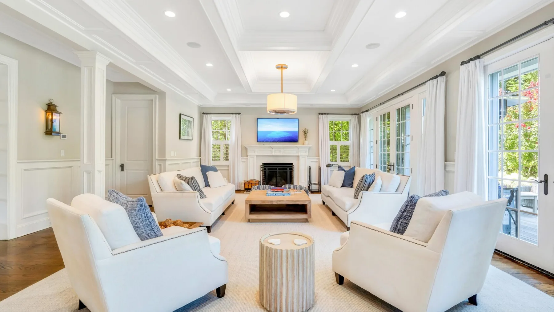 A bright living room with white seating arranged around a fireplace and coffee table.