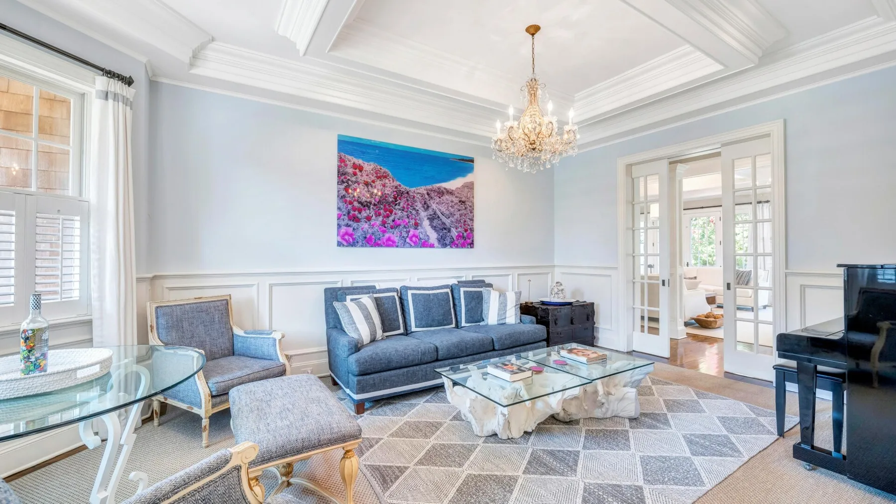 A bright living room with blue seating, a glass coffee table, and a colorful wall print.