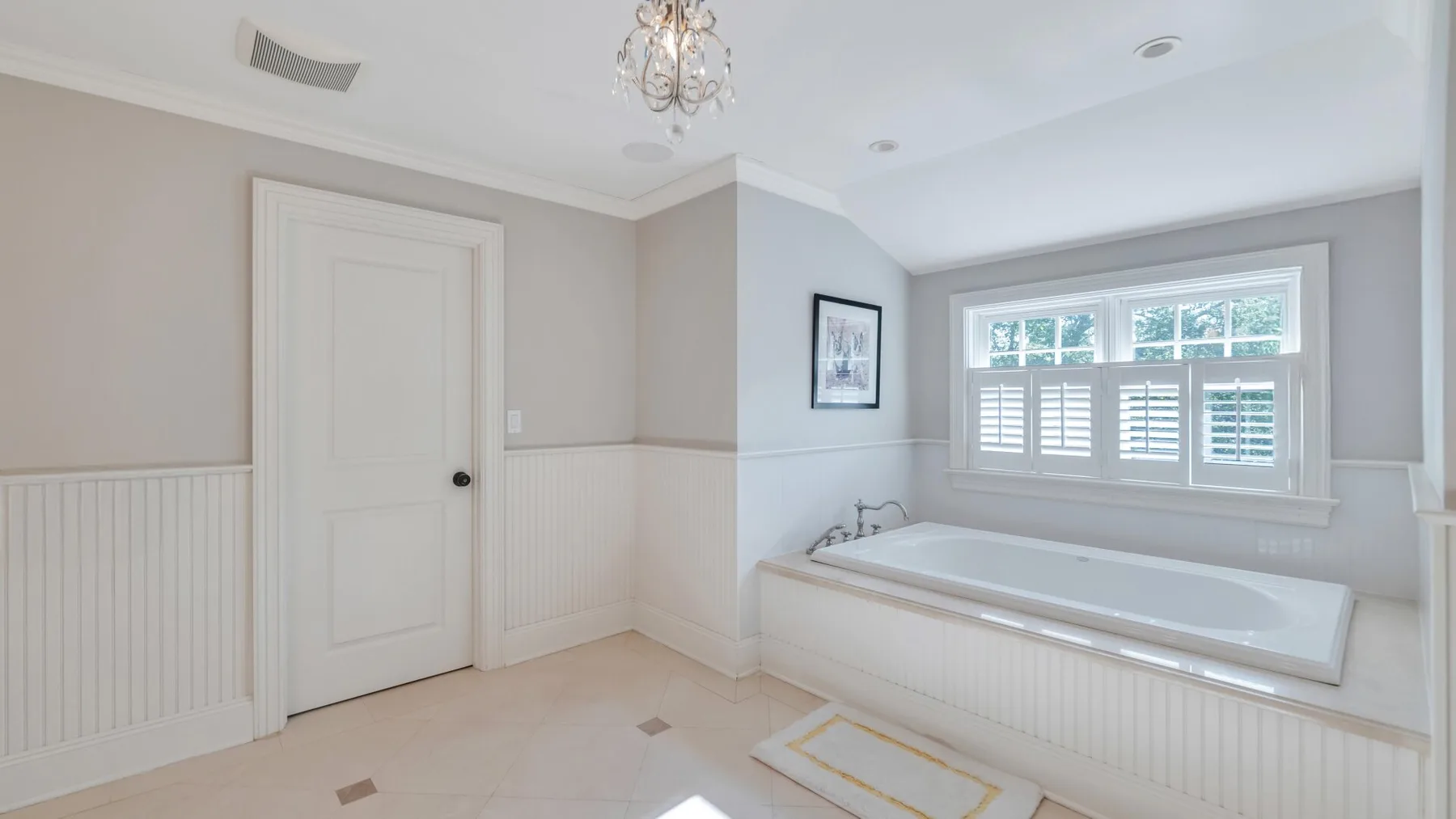 A bright bathroom features a bathtub beneath a window with shutters.