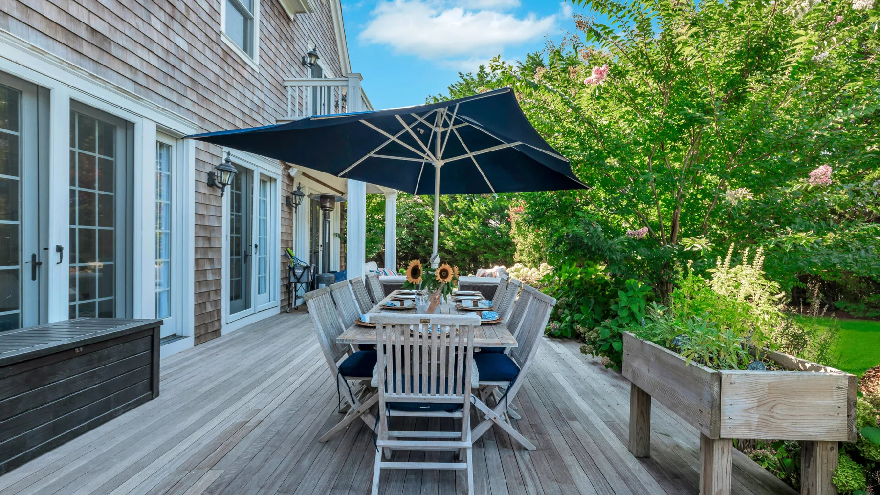 An outdoor dining area on a wooden deck, shaded by a large umbrella.