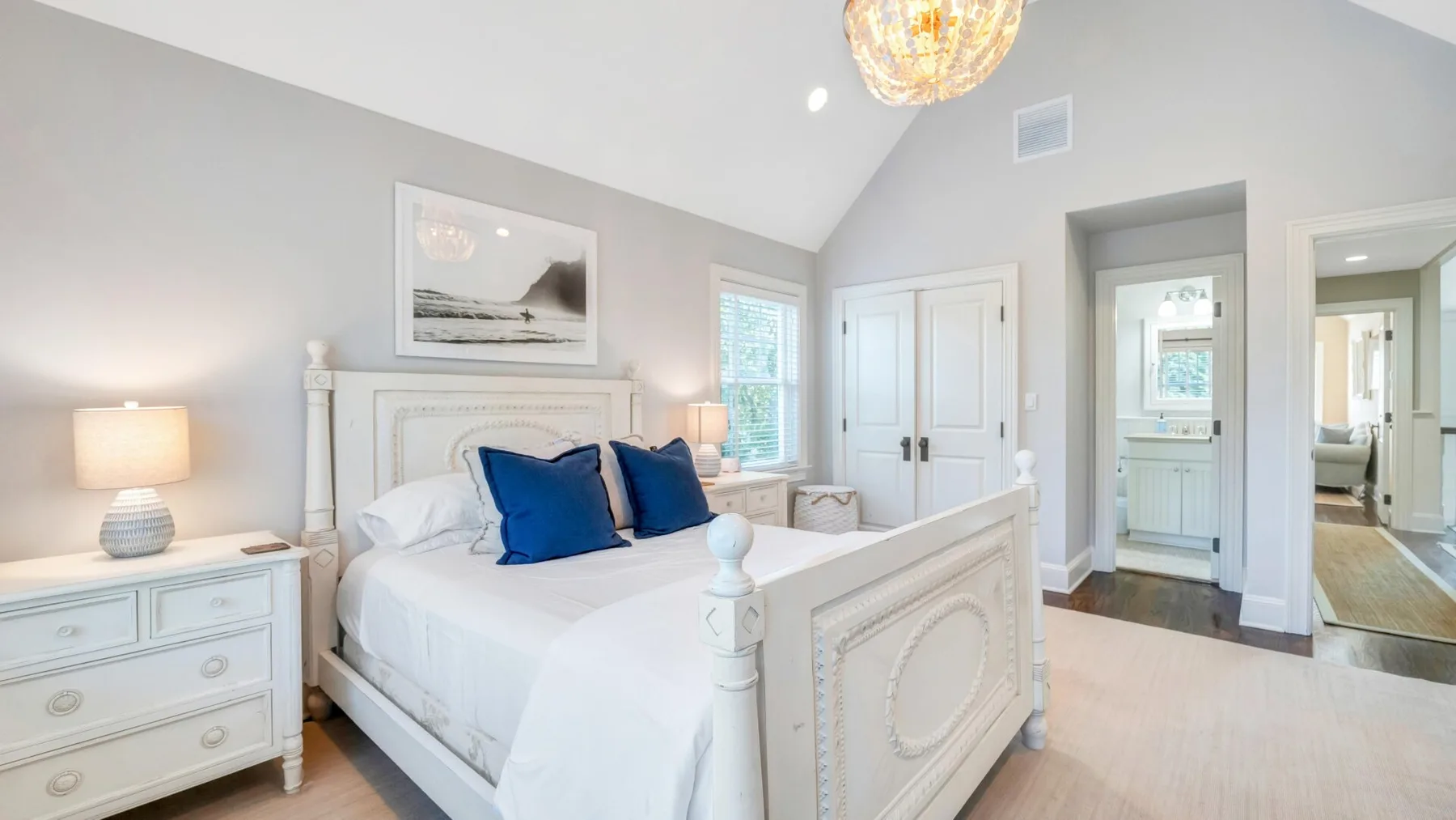 A bright bedroom with a large bed, pale walls, and windows.