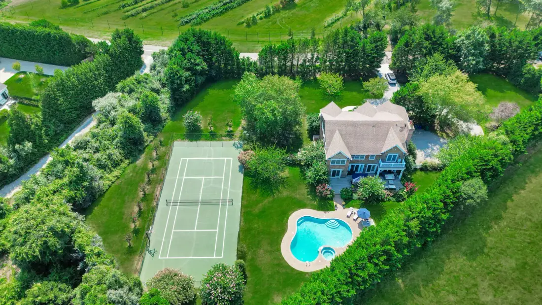 An aerial view shows a house, swimming pool, and tennis court amid green grounds.
