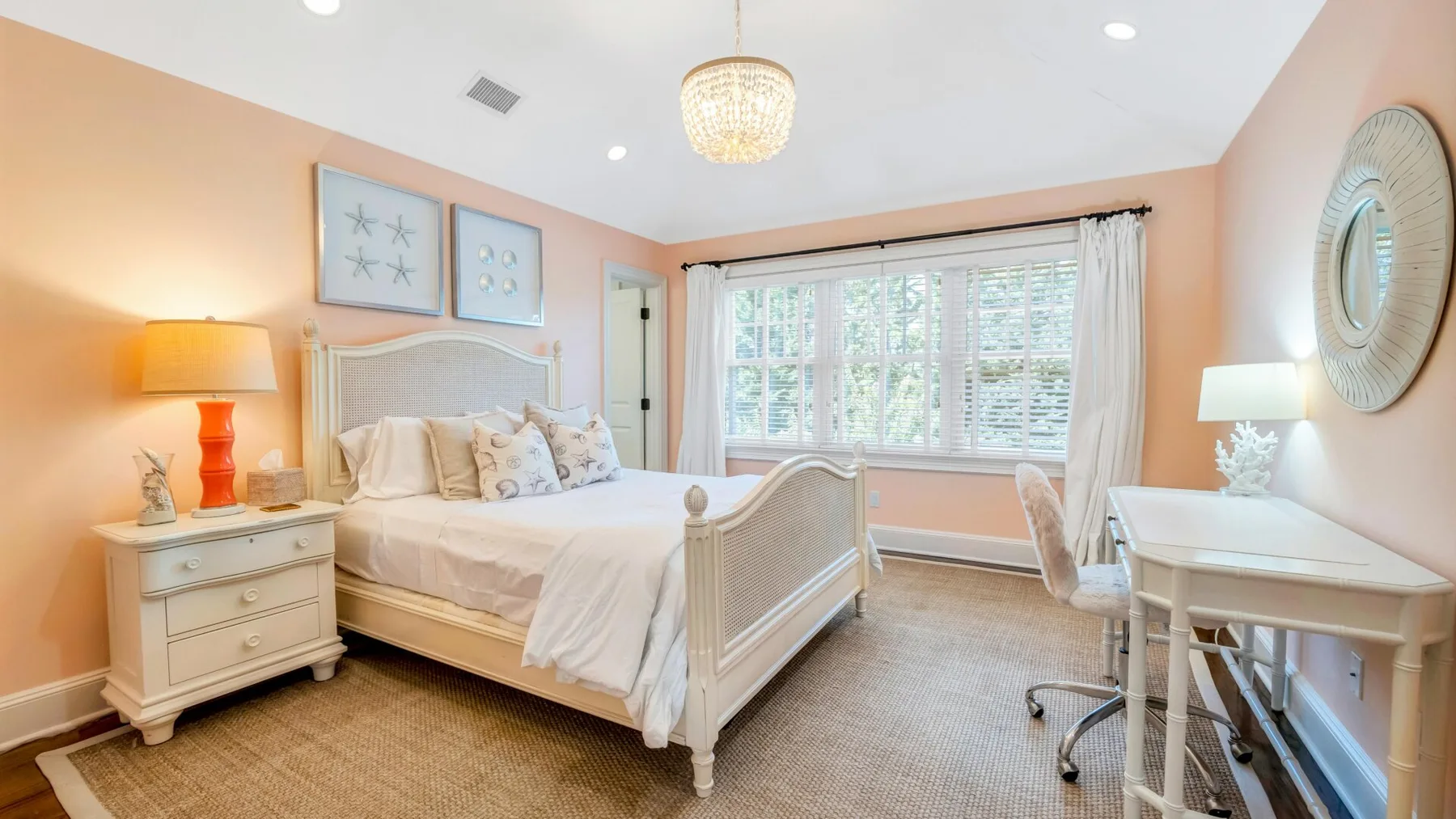 A bright bedroom with a large bed, bedside tables, and a desk by the window.