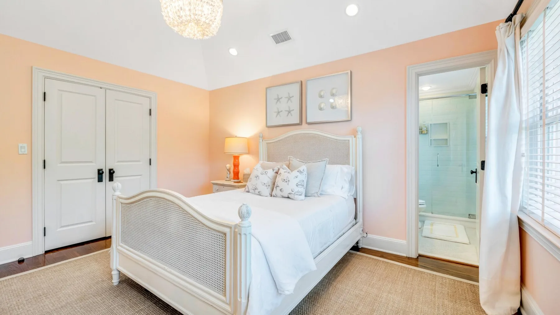 A bedroom with a white bed, peach walls, and a window with curtains.
